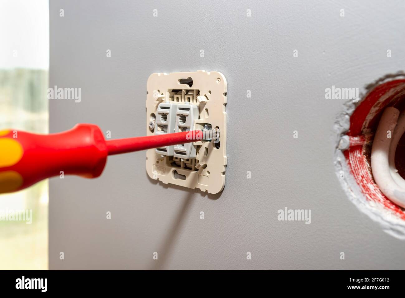 Screwing the switch to the roller shutters up and down with a red screwdriver in the room by the window. Stock Photo