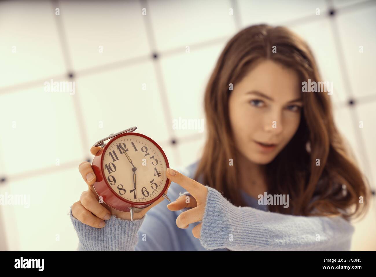 Beautiful young woman showing time on alarm clock. Stock Photo