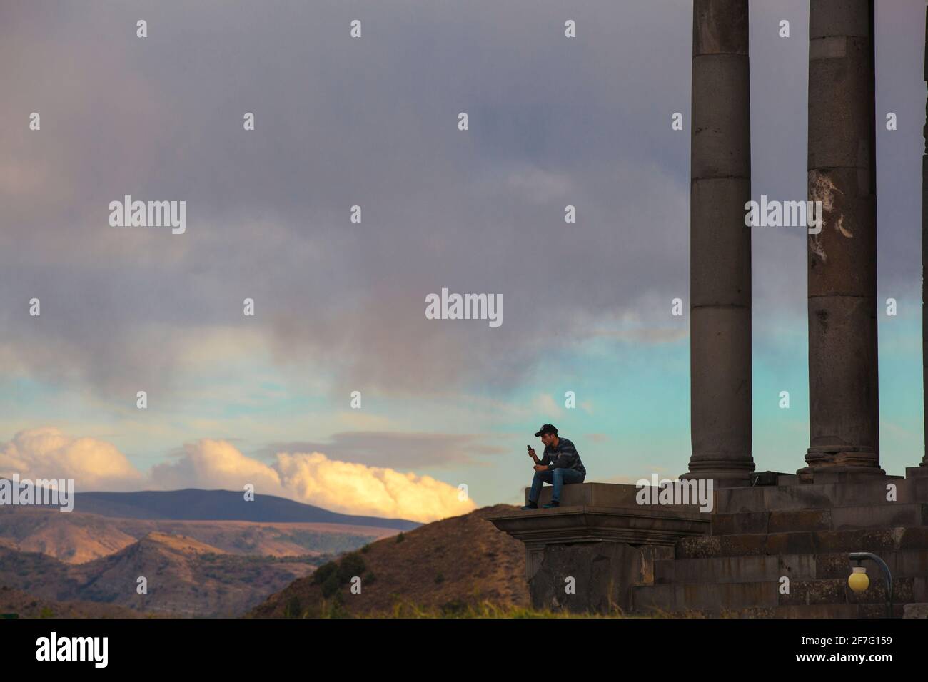 Armenia, Yerevan, Garni, Tourist sitting by Garni Temple looking at mobile phone Stock Photo