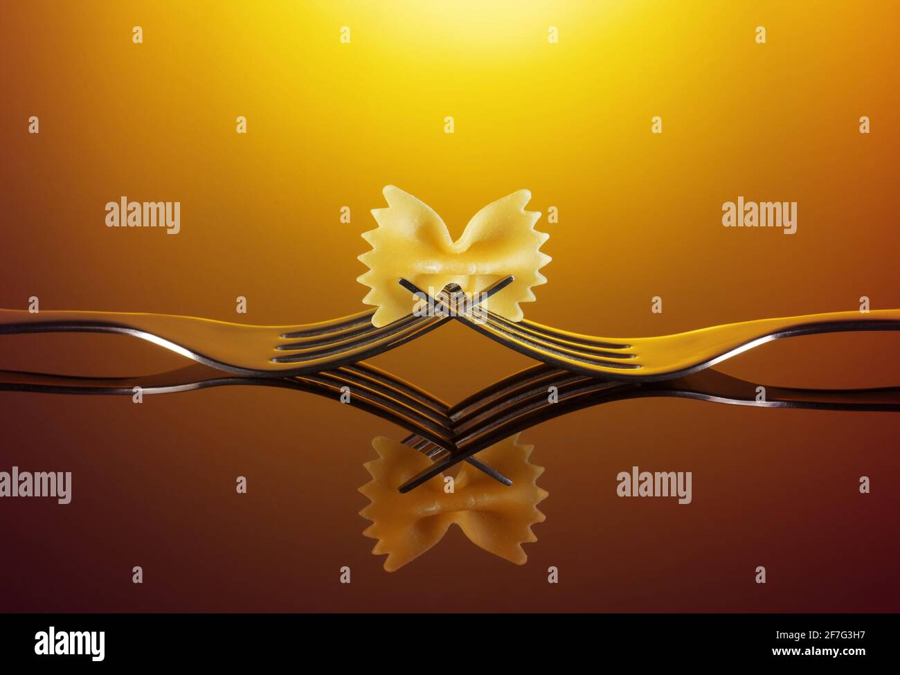 bow tie pasta over intertwined forks on orange background Stock Photo