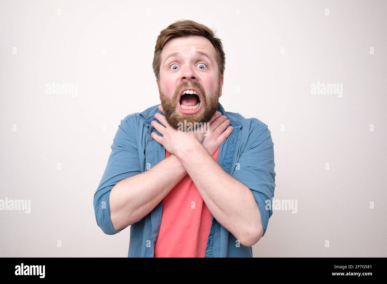 Frightened bearded man suffocates or has a severe sore throat, holding hands on his neck with mouth open. White background. Stock Photo