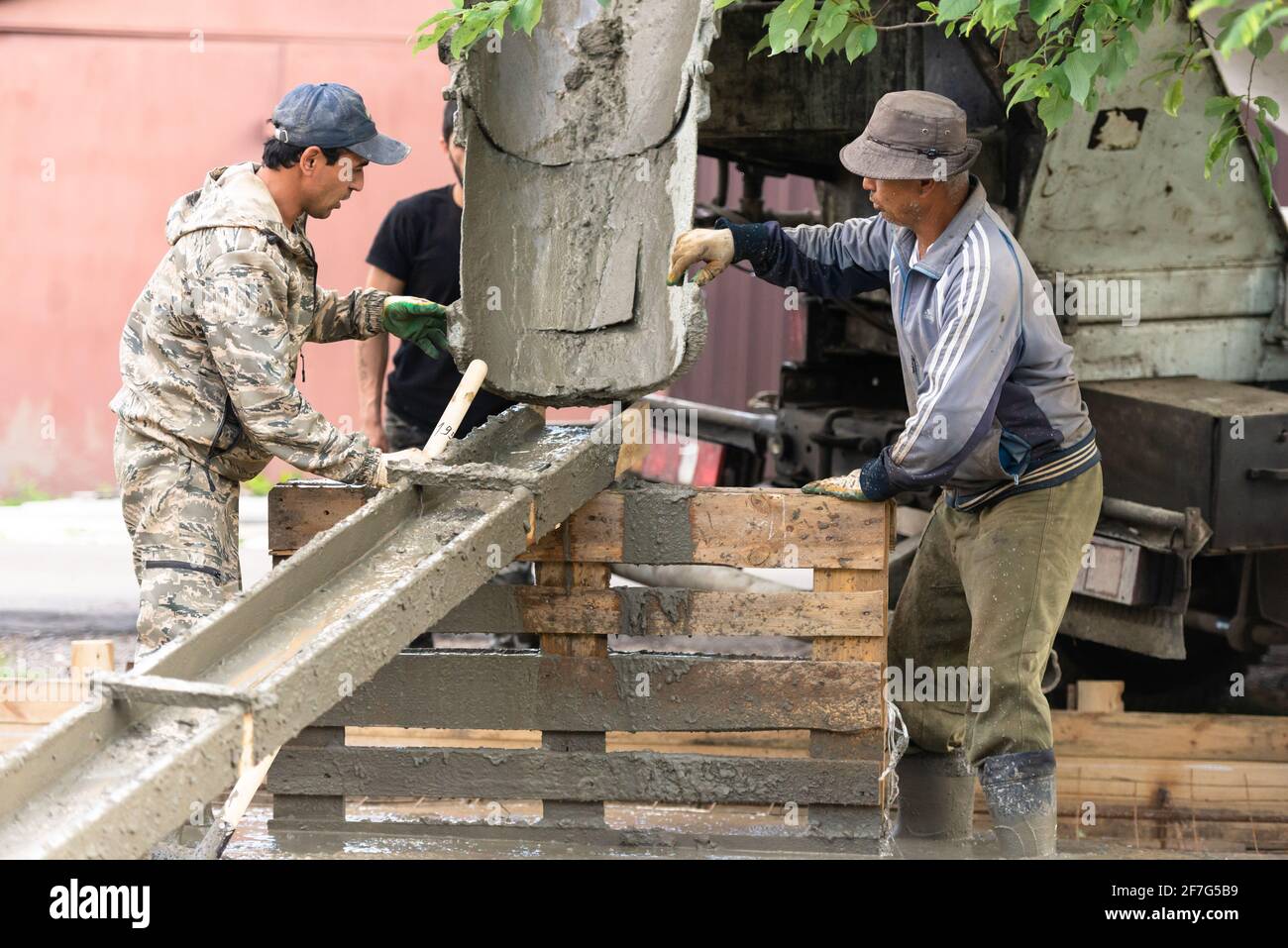 Moscow oblast. Russia. Summer 2019. Pouring concrete slabs. Two workers prepare a tray for draining concrete from a concrete mixer. Stock Photo