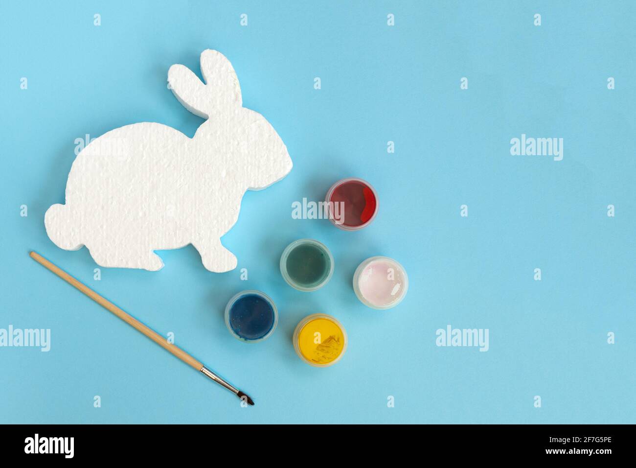 White figure of bunny or rabbit for decorating, paints and brushe on blue background. Easter diy with children. Top view with copy space. Stock Photo