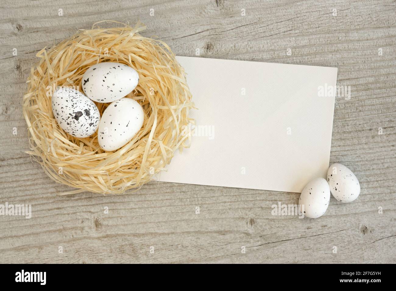 Easter eggs in a straw nest and greeting card over white wood. Template ...