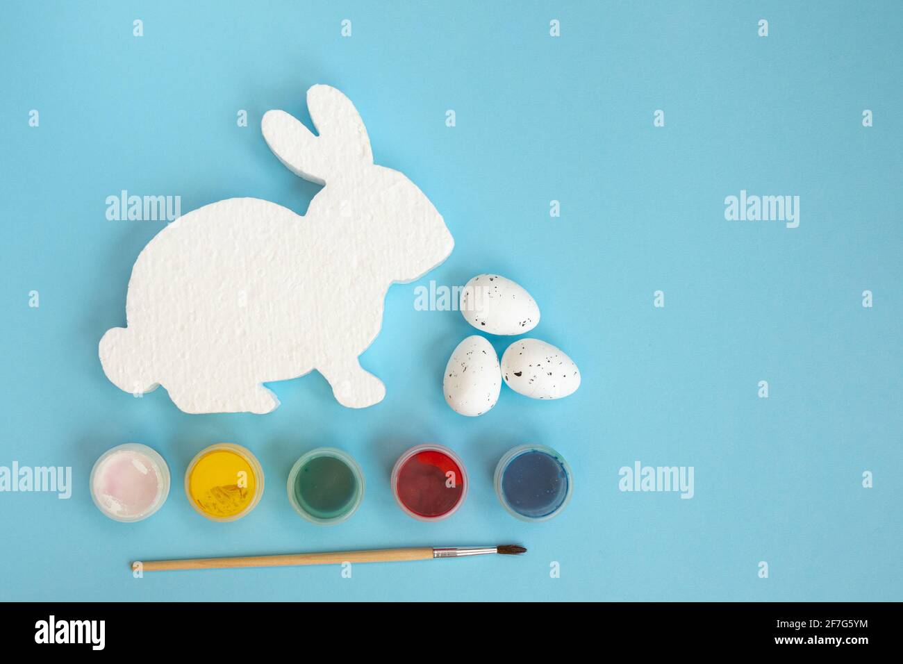 White figure of bunny or rabbit for decorating, paints and brushe on red background. Easter diy with children. Top view with copy space. Stock Photo