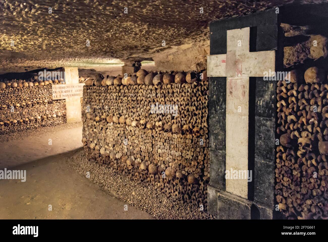 Tunnel with stack of skulls and bones and white crosses in the catacombs of Paris, France Stock Photo