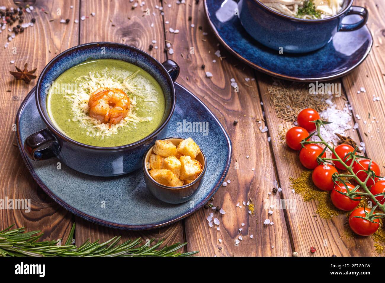 Mashed soup with shrimp, croutons and cherry tomatoes on a brown wooden background decorated with spices, rosemary, coarse salt. Top view. Stock Photo