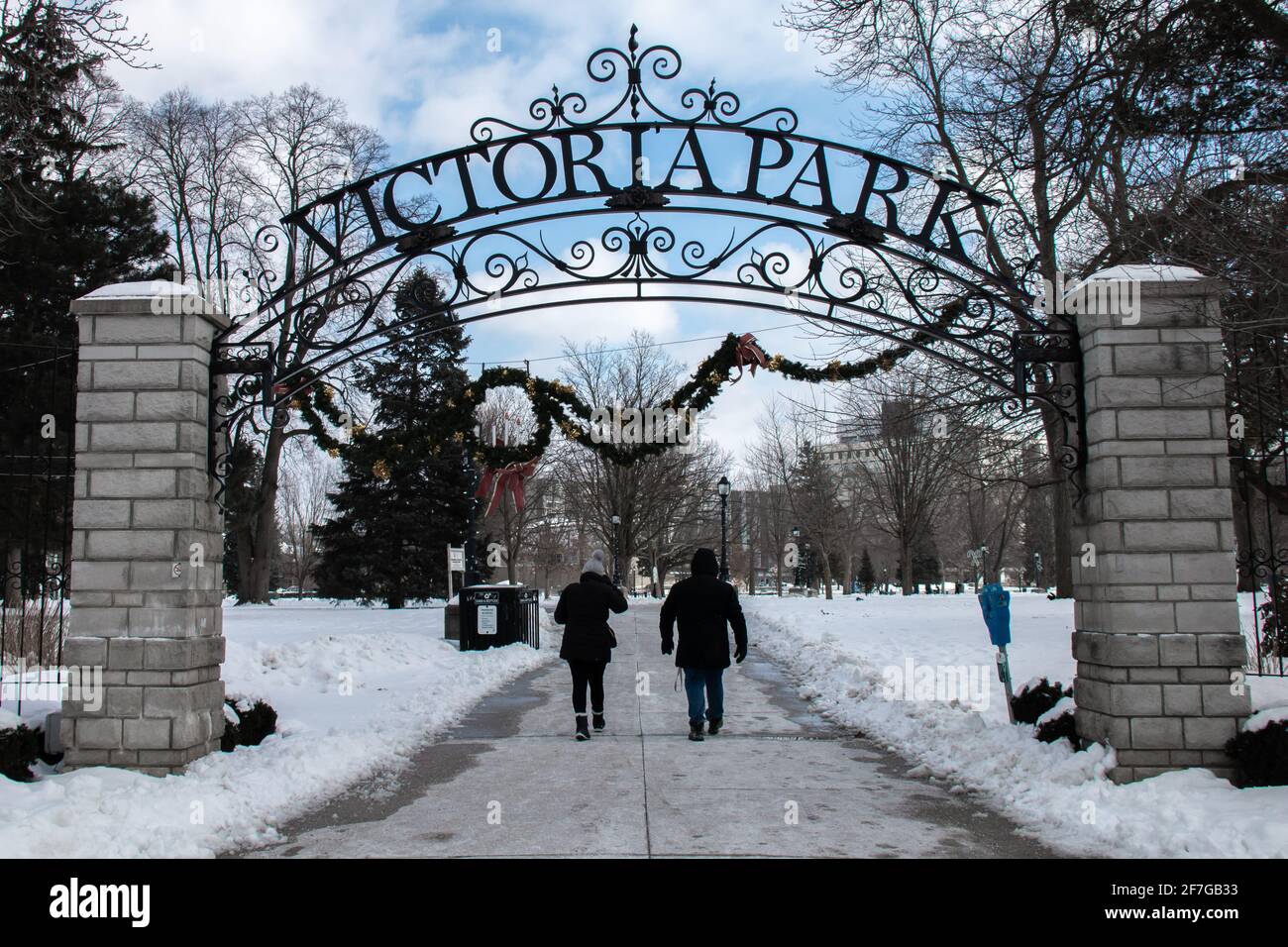London, Ontario, Canada - February 6 2021: A couple walks under the iron wrought sign at Victoria Park's entrance in February during COVID-19 lockdown. Stock Photo
