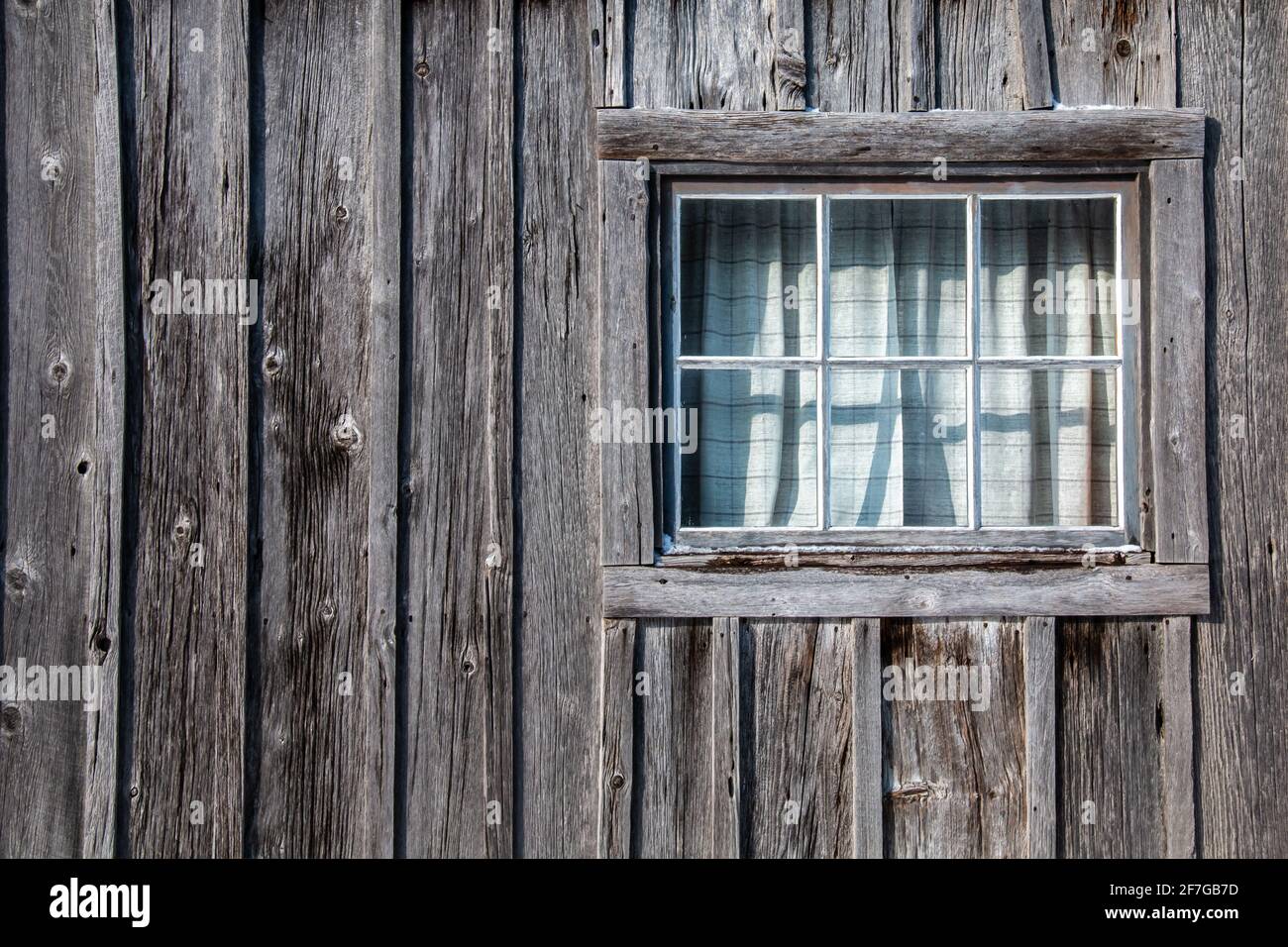 An old settler home in Lucan, Ontario, with worn wooden planks and a cute window with plaid curtains, photographed February 2021. Stock Photo