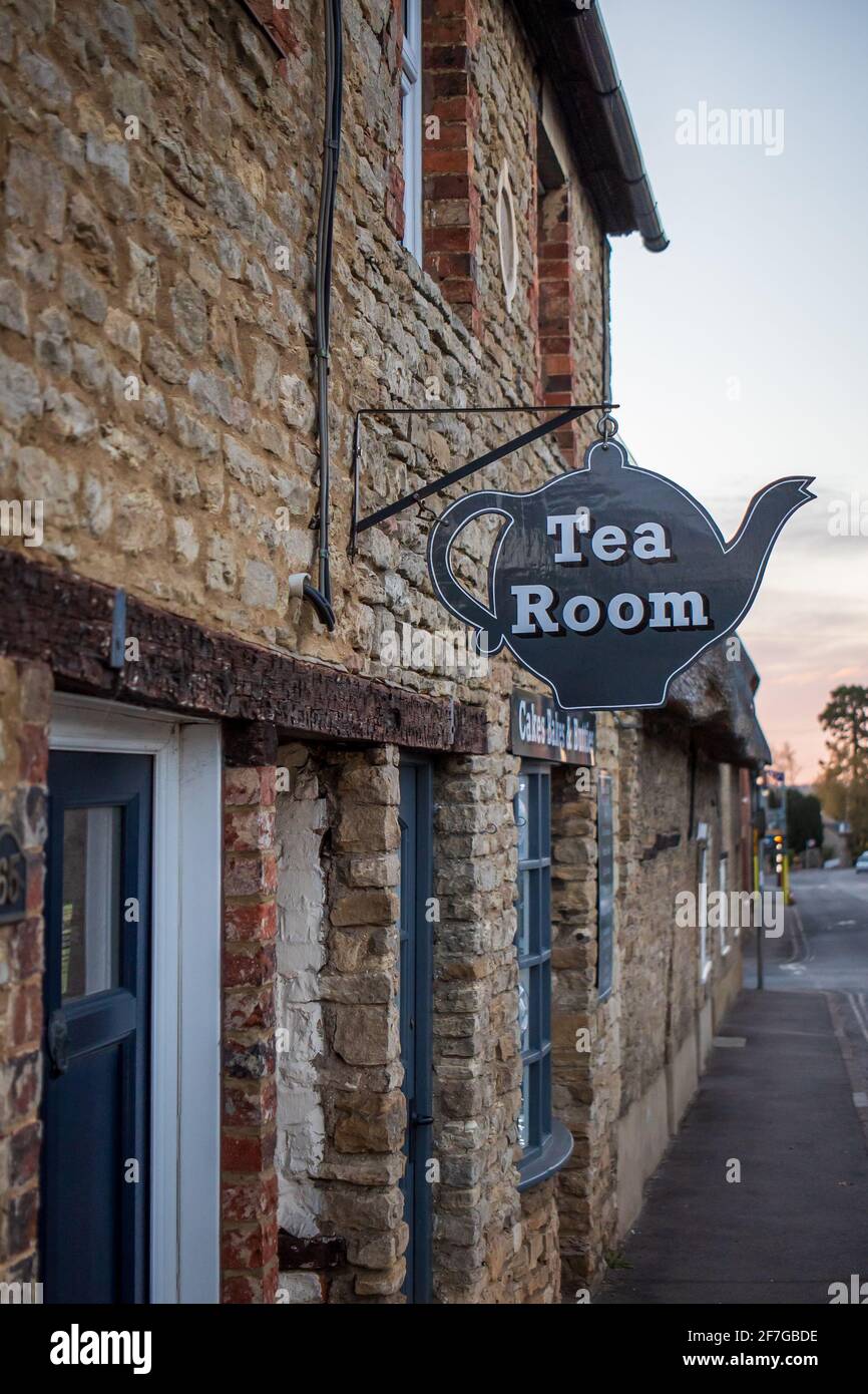 Sharnbrook village high street, Bedfordshire, England, UK - Thatched cottage tea room with hanging teapot sign at sunrise Stock Photo
