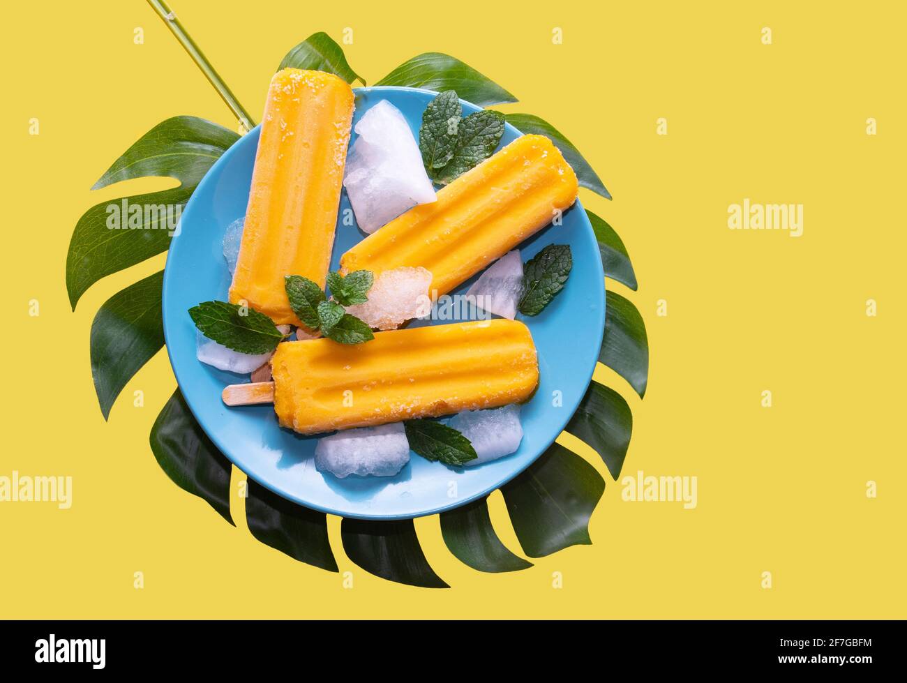 Delicious fresh mango popsicle served with mint leaves and ice cubes, cold fruity and healthy dessert, mango ice cream isolated on yellow background Stock Photo