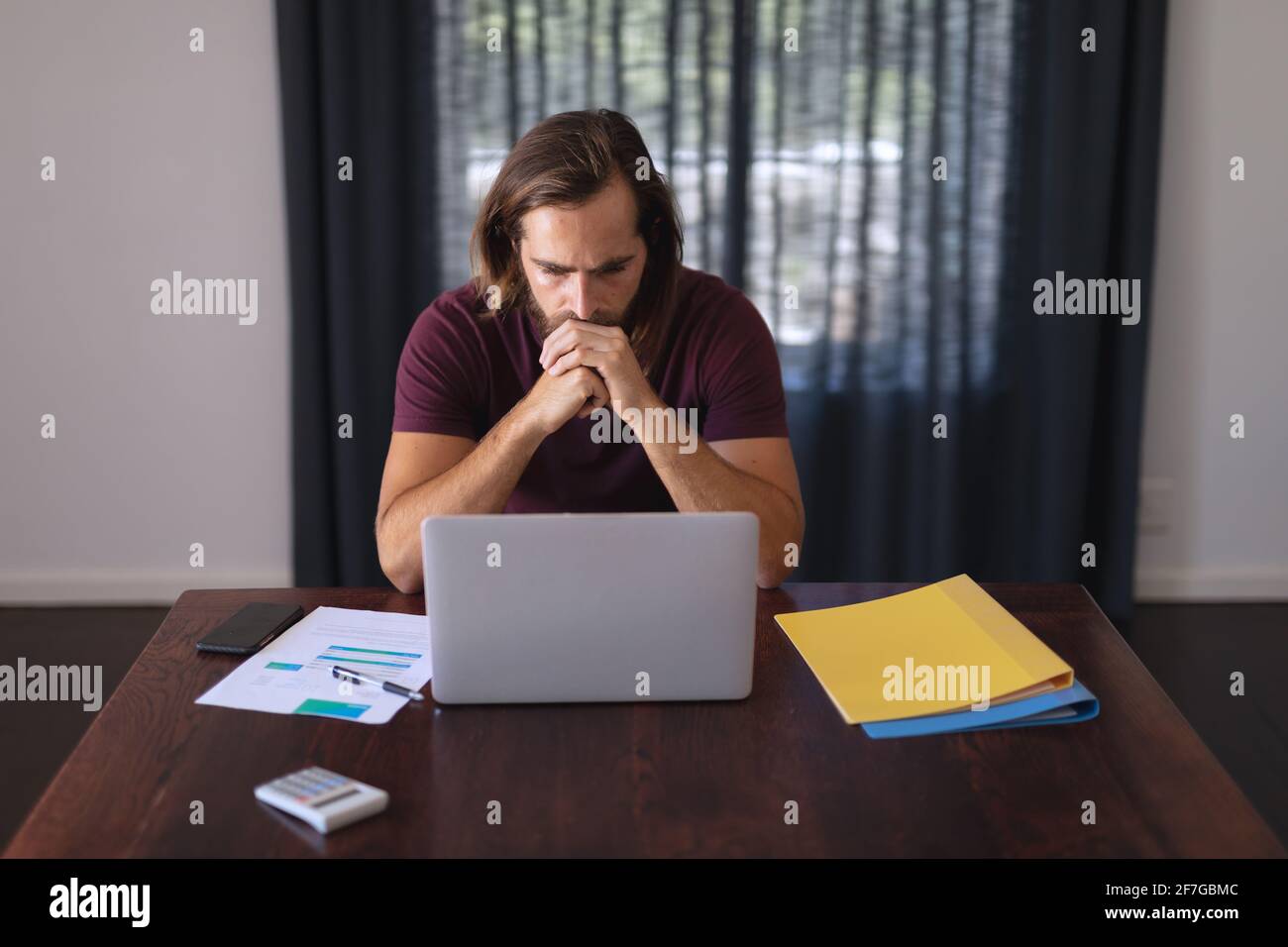 Worried caucasian man sitting at table working from home and looking at laptop screen Stock Photo