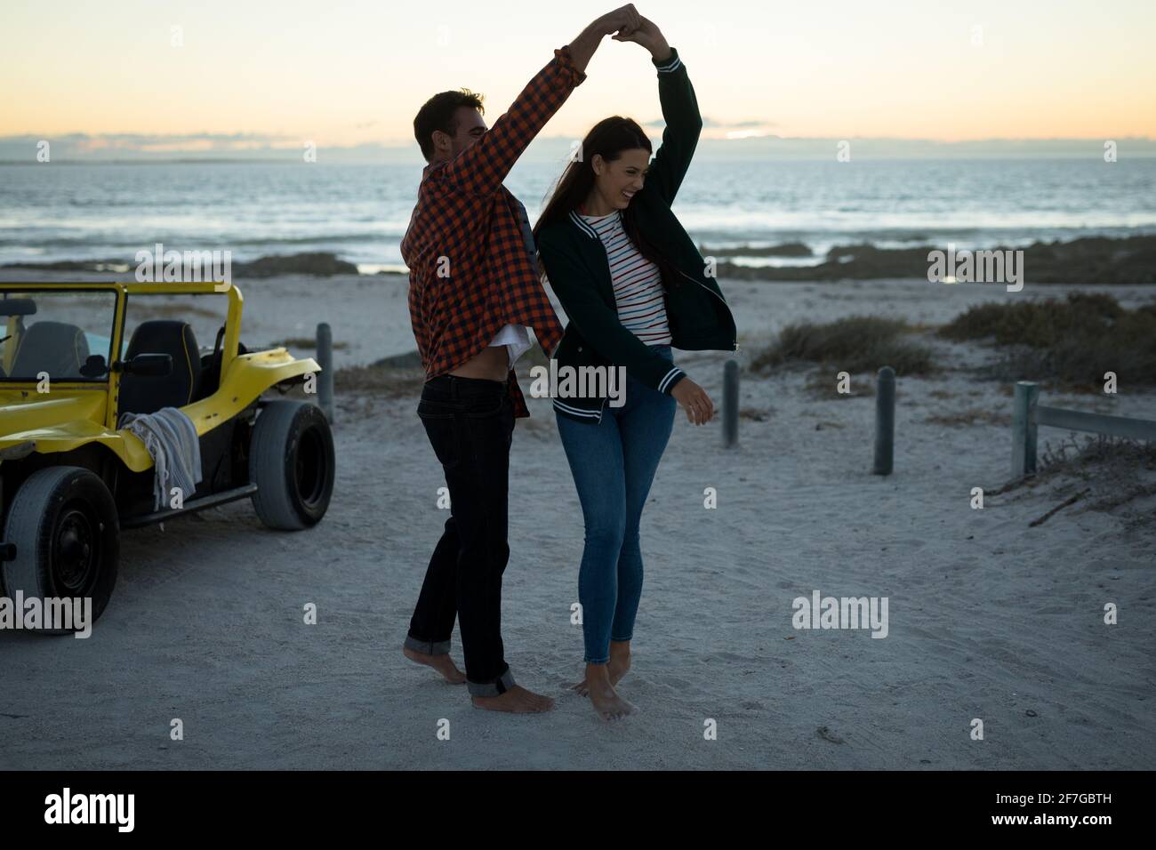 Happy caucasian couple next to beach buggy by the sea dancing Stock Photo