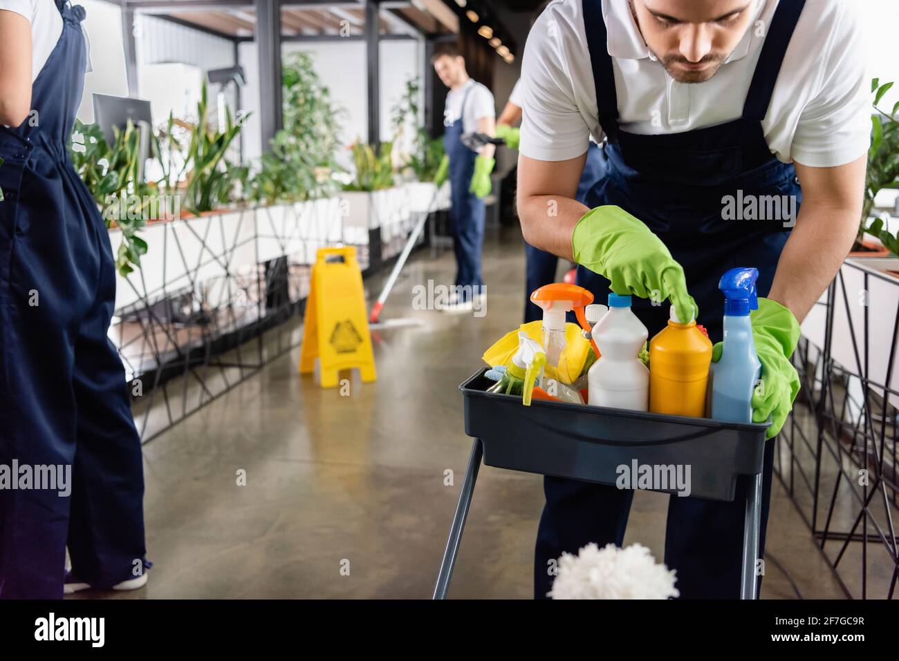 Worker of cleaning service opening detergent near colleagues in office ...