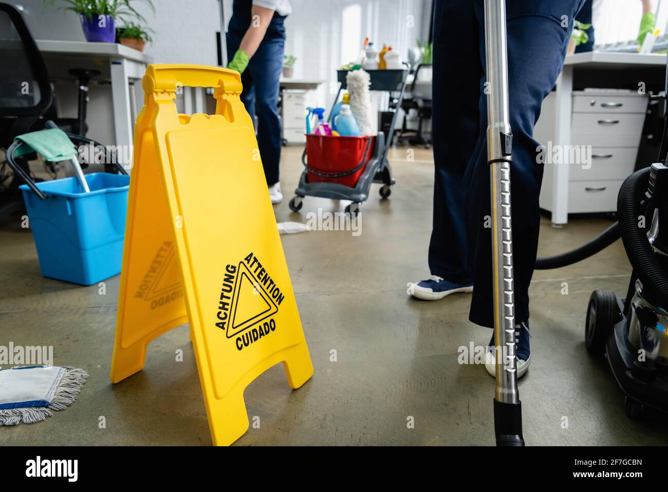 Cropped view of cleaner standing near wet floor signboard in office Stock Photo