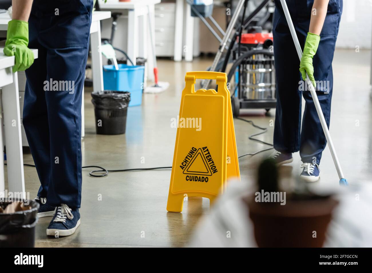 Cropped view of wet floor signboard near cleaners working in office Stock Photo