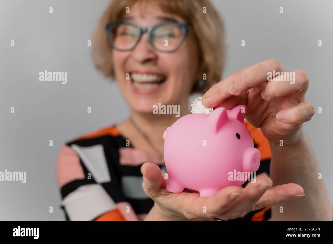 Happy elderly woman puts coin in piggy bank on white background Stock ...