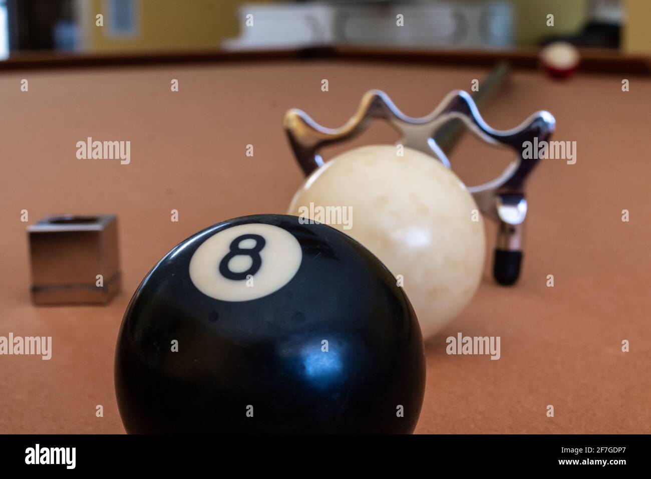 A billiards bridge aid, white ball, eight ball and cue chalk line up on a gold felt pool table, Toronto, Ontario Canada. Stock Photo