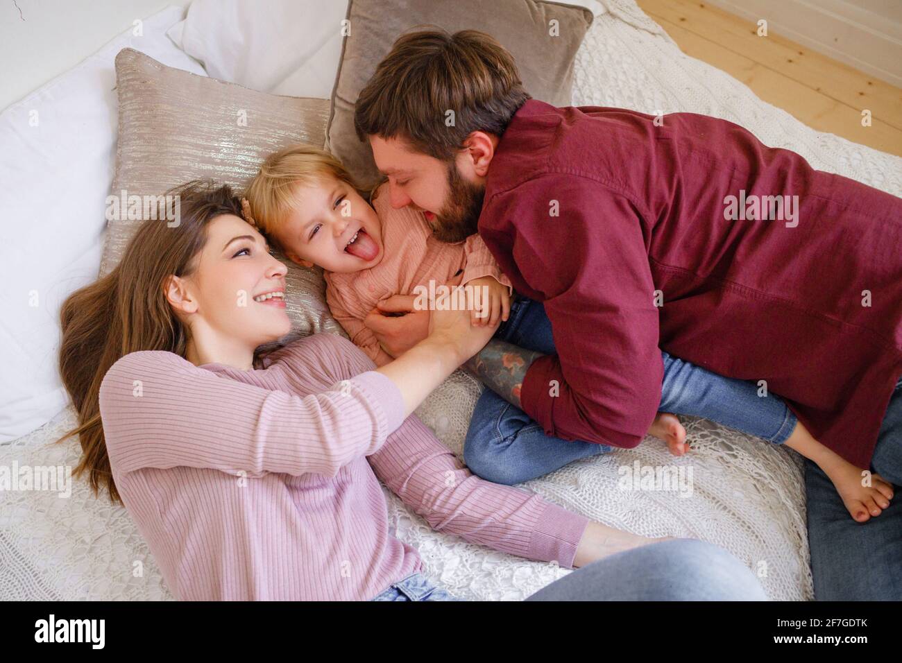 Family plays with the child on the bed. Mother and father laugh with little daughter.  Stock Photo