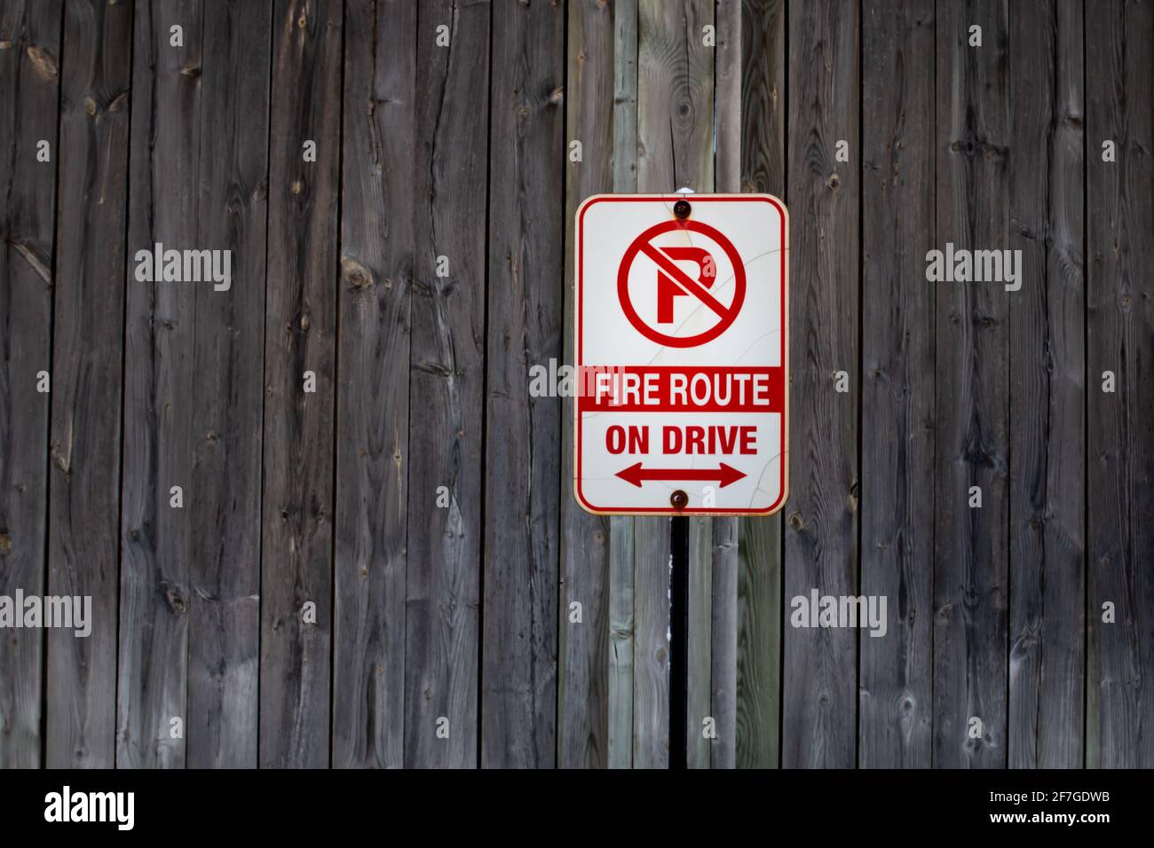 A vertical and rectangle shaped no parking sign signifying a fire route is tacked up to a weathered wooden fence in London, Ontario, Canada, February. Stock Photo