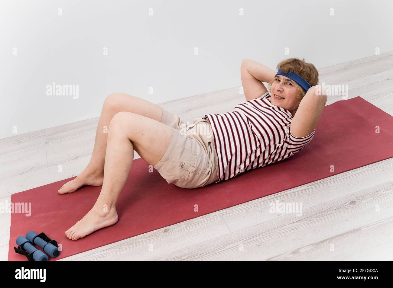 Happy old woman doing abs exercises on a sports mat. Elderly lady doing