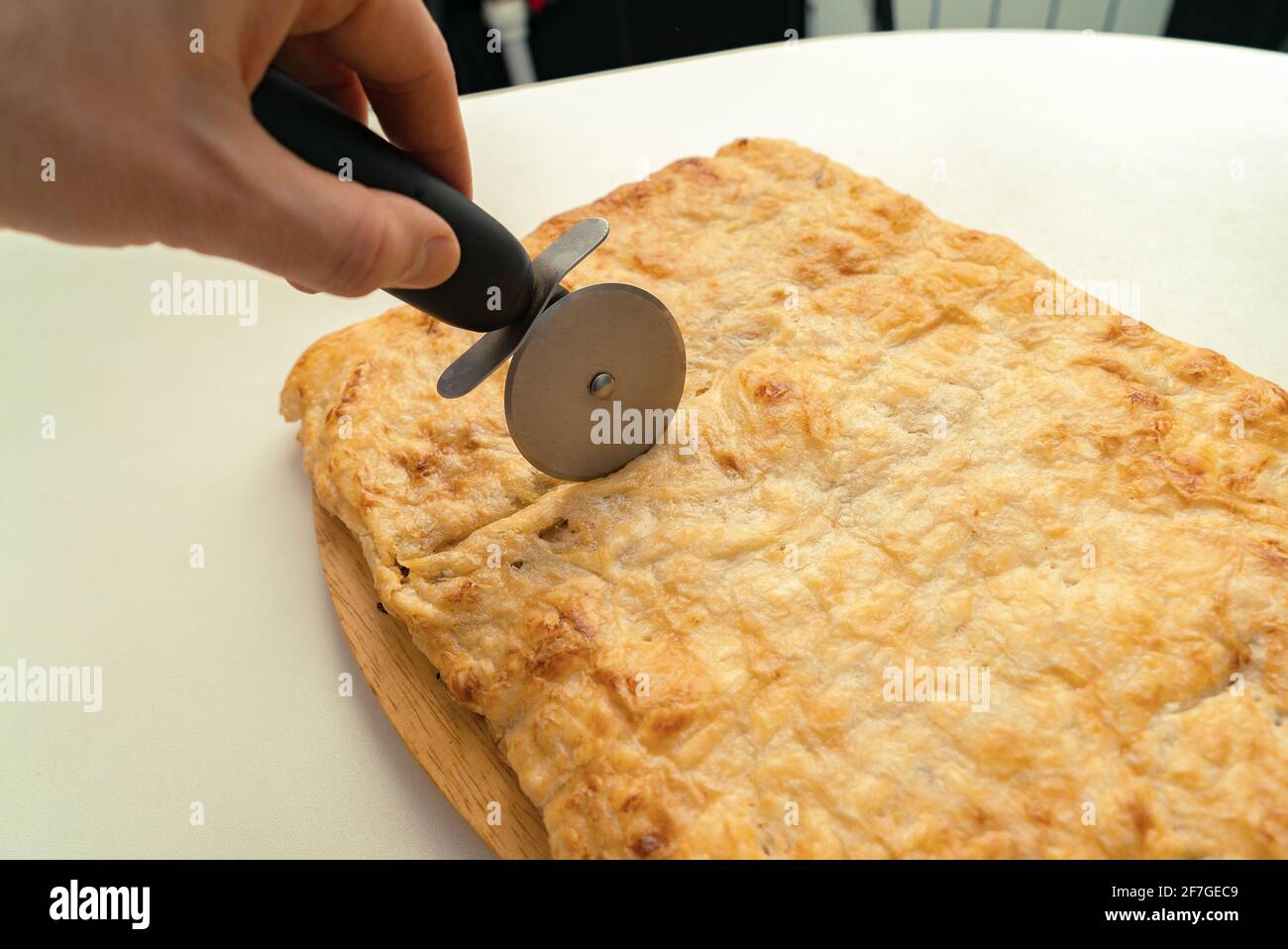 Human hand cutting the finished baked pie with a circular knife on