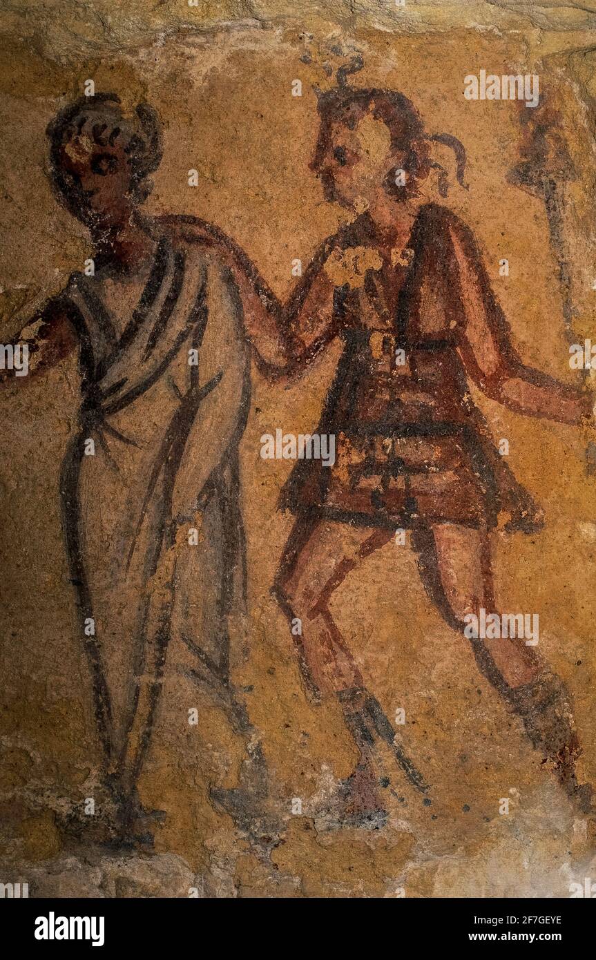 Vanth (right), female demon of the Etruscan Underworld, dressed as a  huntress in a short tunic and boots and holding a torch aloft, guides a  woman to the afterlife. Detail of wall