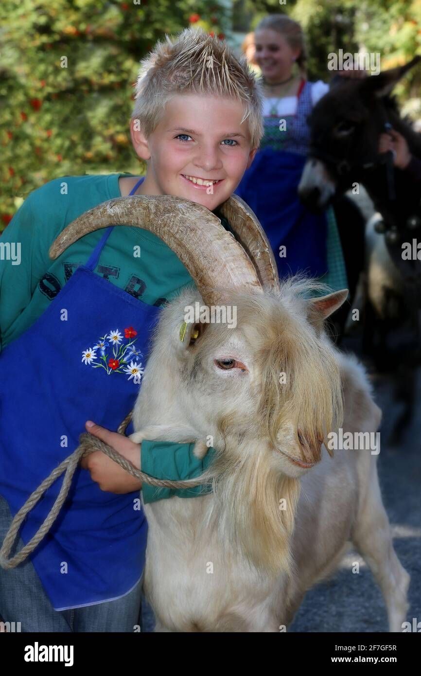 freudiger Junge mit Tracht führt Ziege  beim Almabtrieb ins Tal in Südtirol in den Dolomiten in Italien Stock Photo