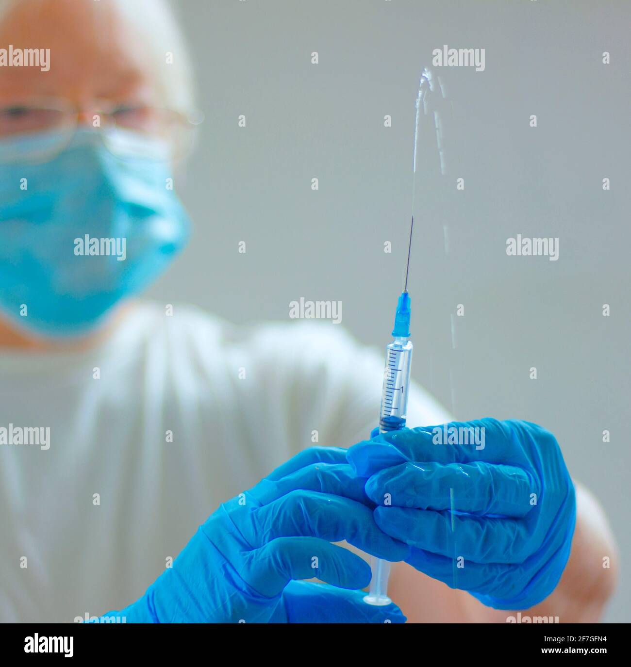The vaccine against the coronavirus CAVID-19. a female doctor in a mask and blue medical gloves and a syringe with a vaccine is vaccinating. the conce Stock Photo