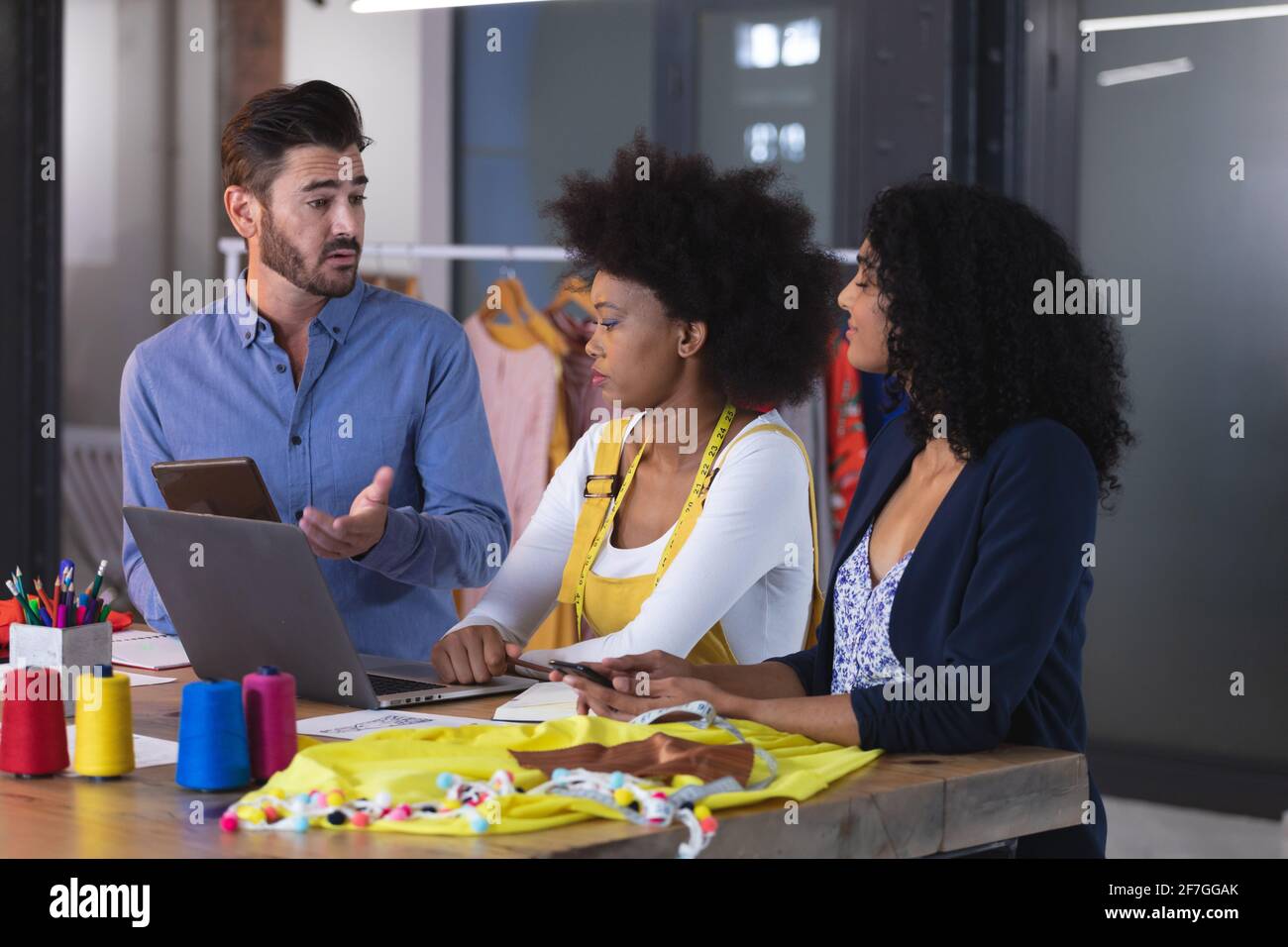 Diverse group of fashion designer colleagues in discussion at work using digital tablet Stock