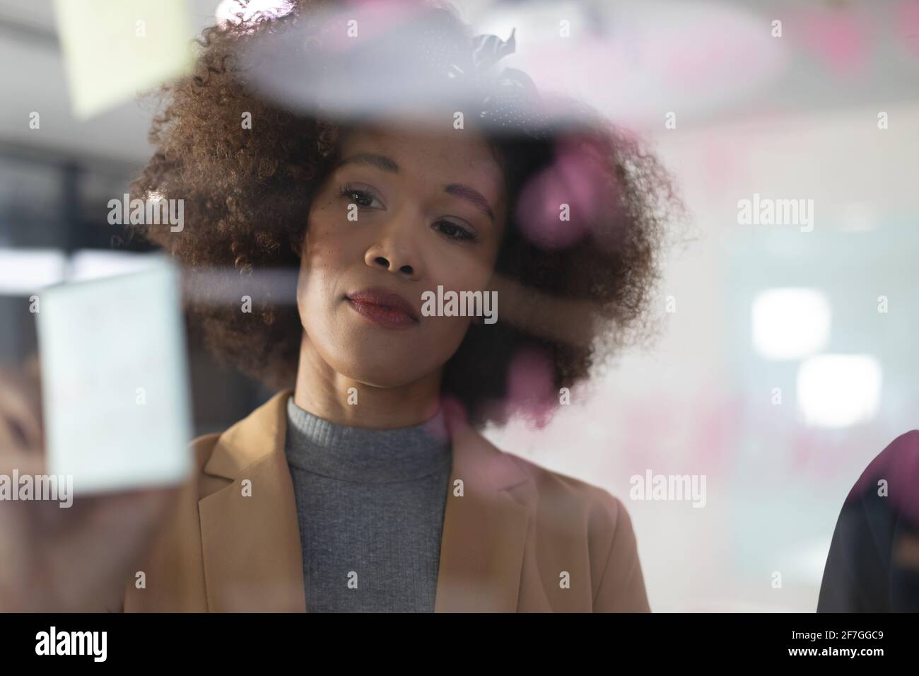 Smartly dressed african american businesswoman writing notes on glass wall at the office Stock Photo