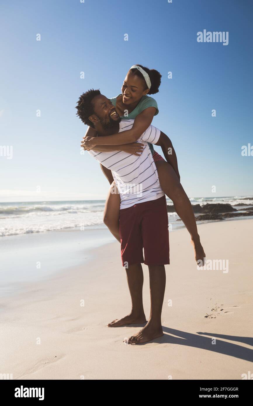 Happy african american couple on the beach piggybacking looking at each other Stock Photo