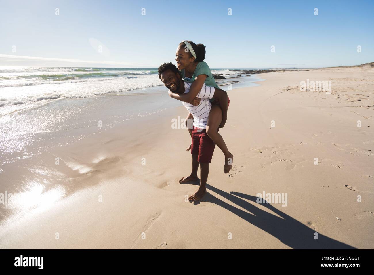 Happy african american couple on the beach piggybacking Stock Photo