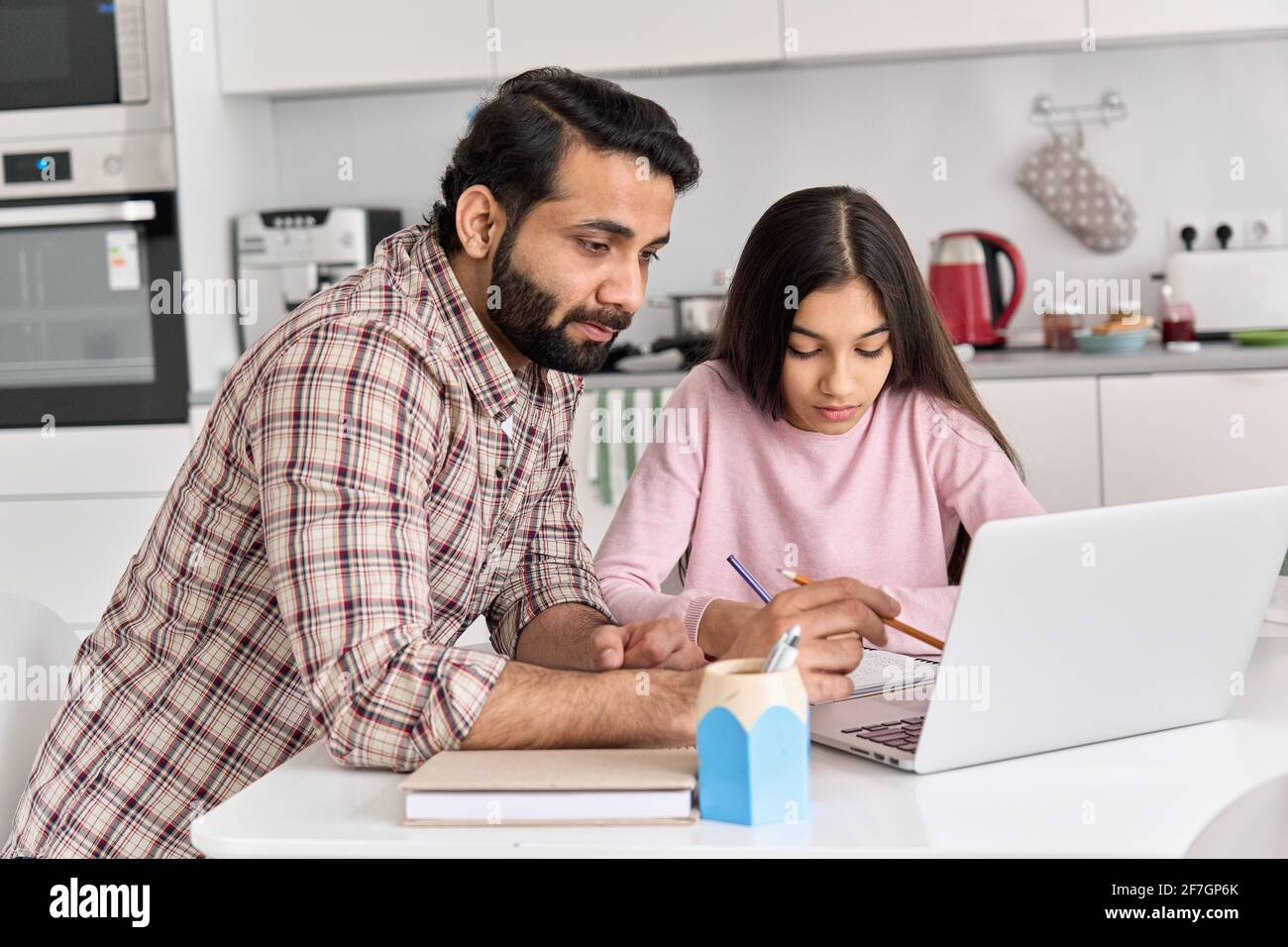 Young indian father helping school child teen daughter studying online at home. Stock Photo