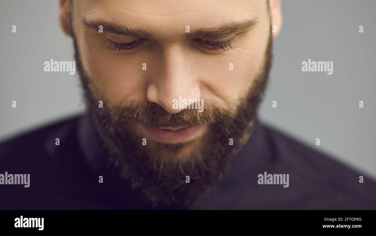 Studio close up portrait of handsome bearded man looking down with eyes half closed Stock Photo