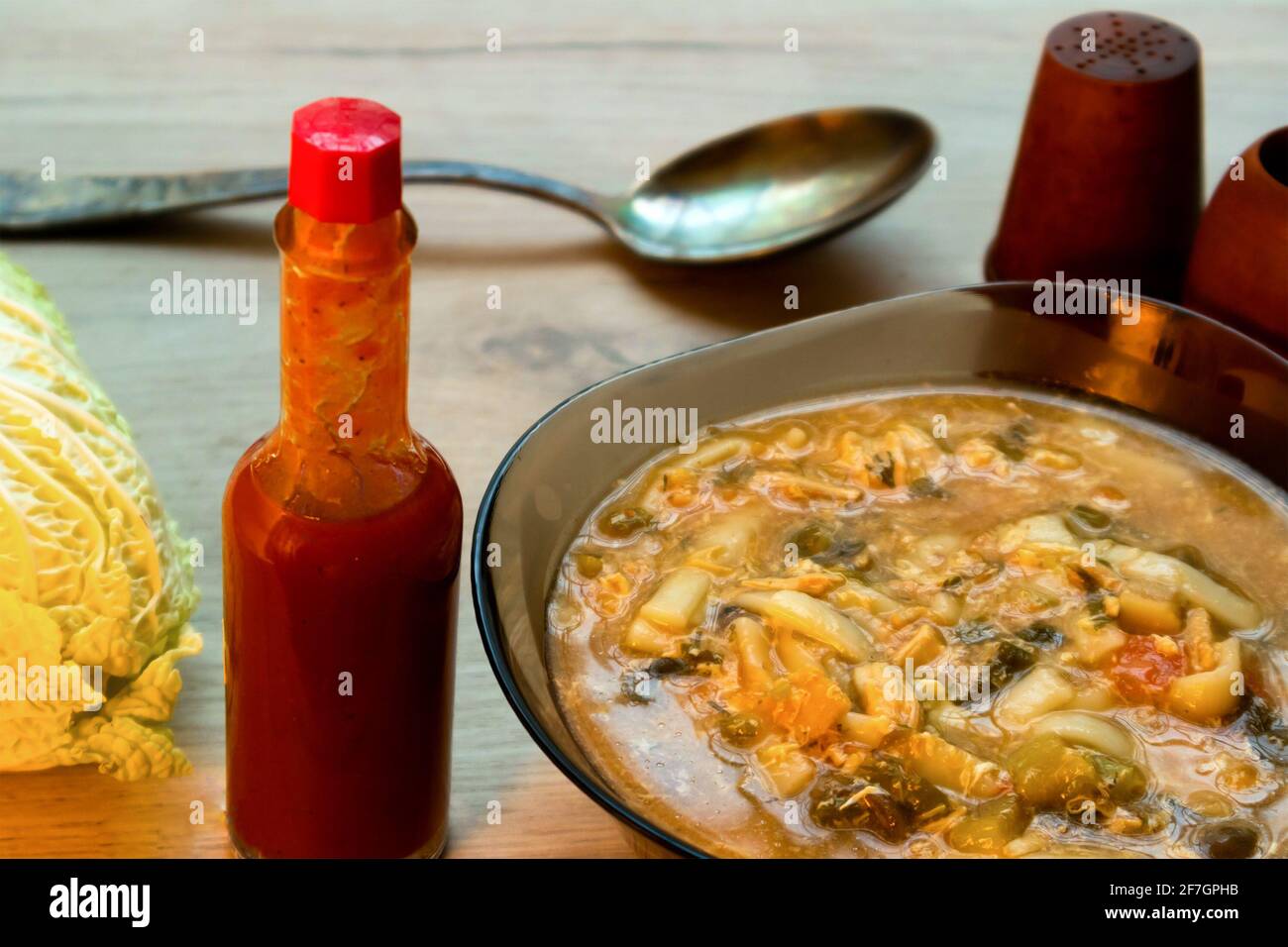 Spicy asian noodle soup in a glass bowl, tabasco sauce and chinese cabbage served on a wooden board Stock Photo