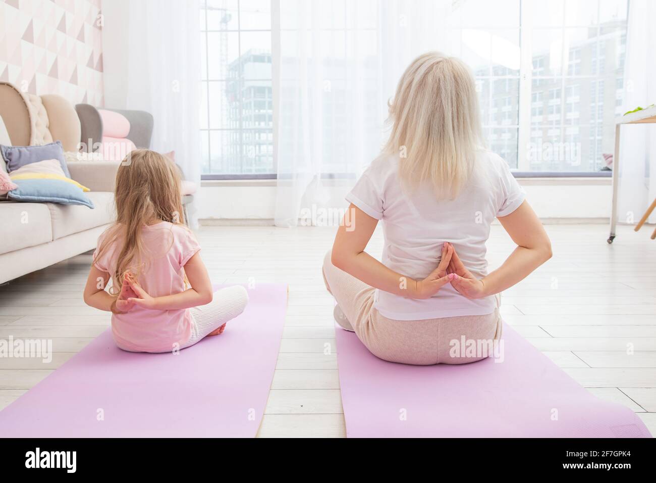 Full length back side view smiling blond mother on yoga mat with