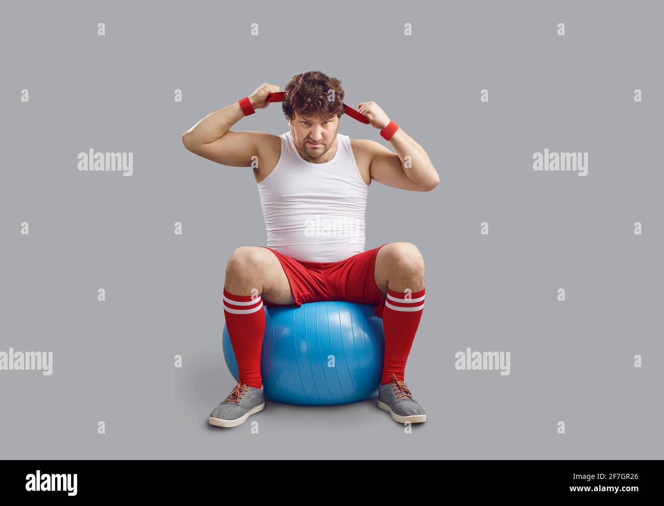Funny angry chubby man sitting on fitness ball and getting ready for gym workout Stock Photo