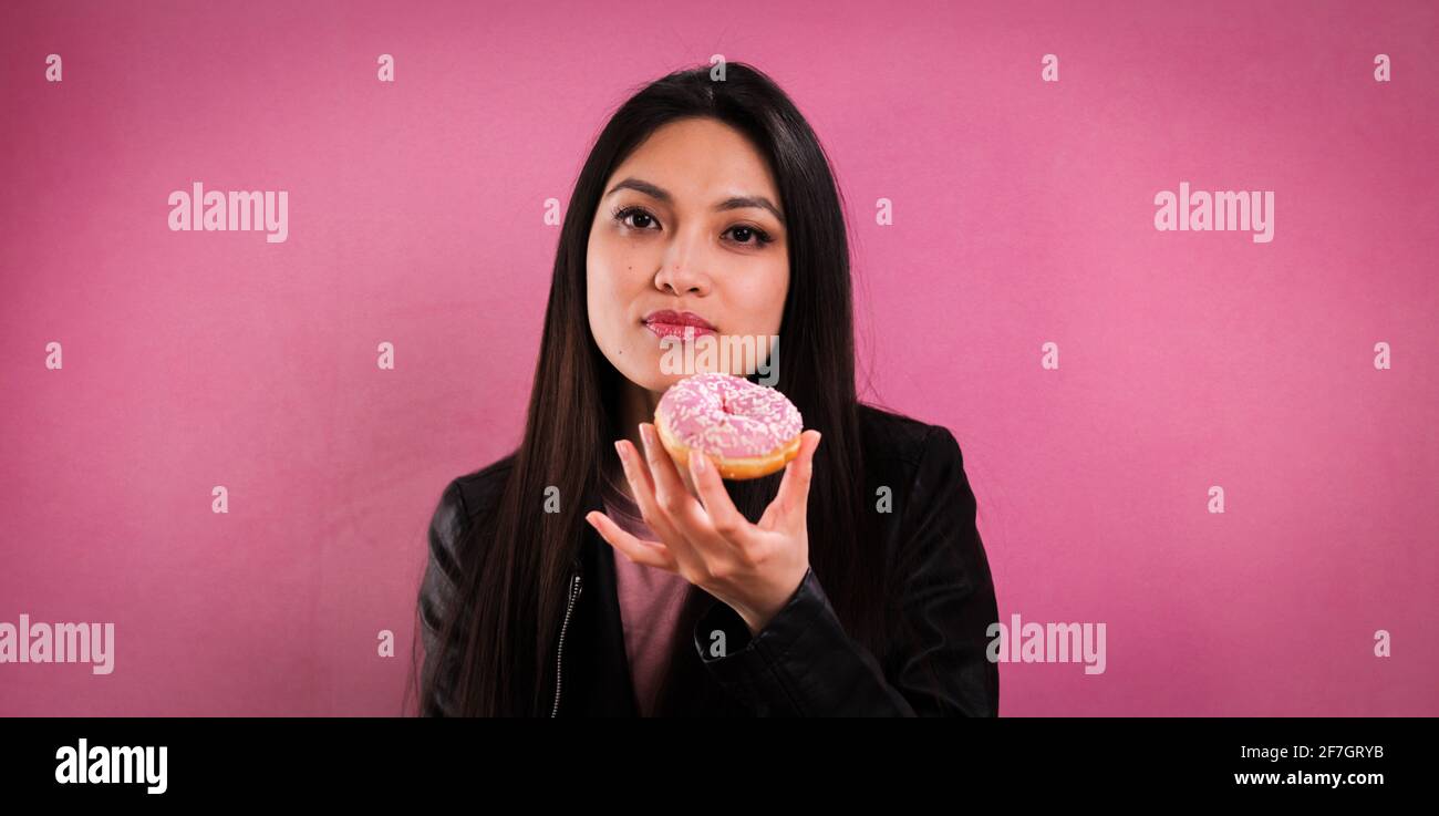 Young woman eats a doughnut against a pink background Stock Photo