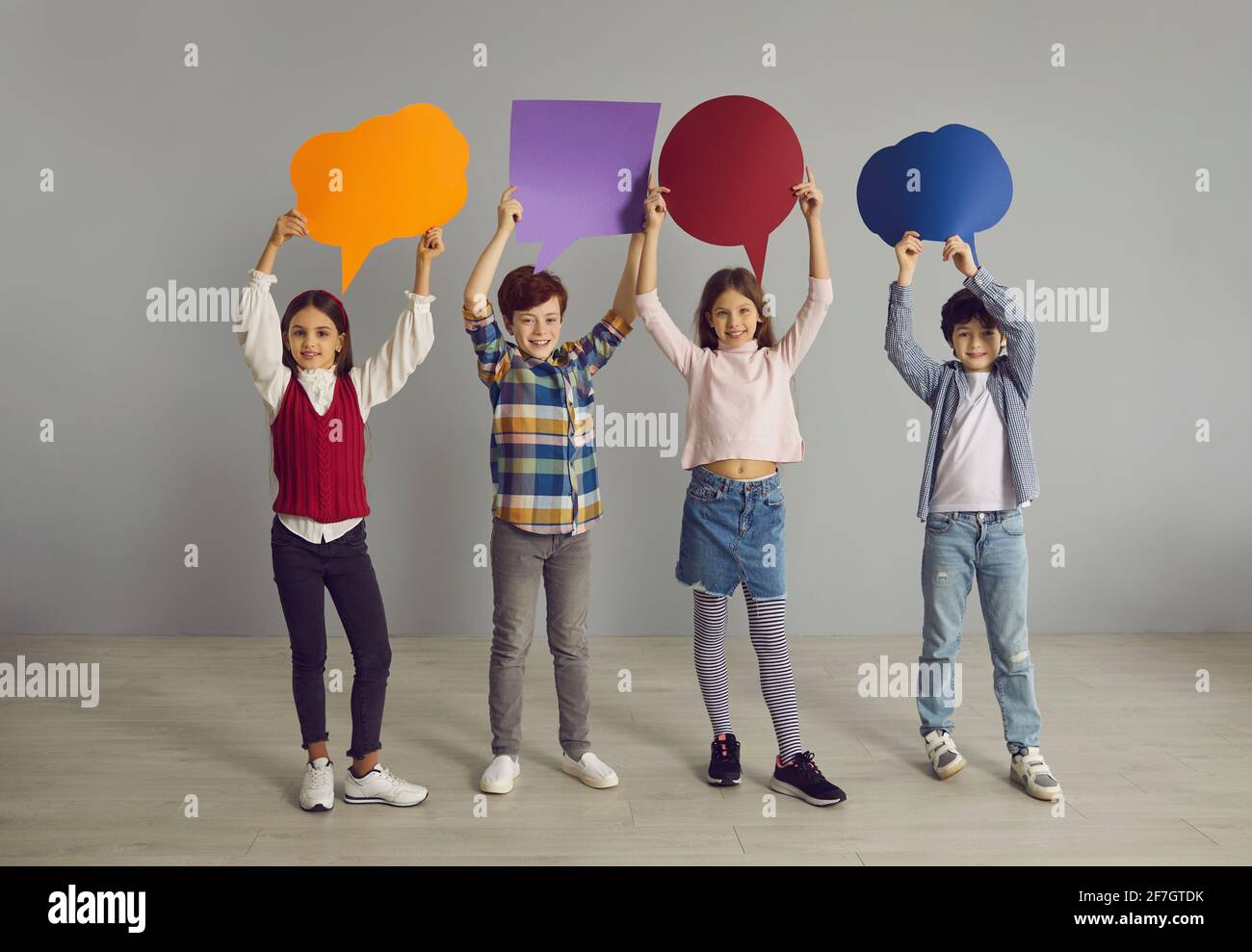 Group of happy little school children holding up multicolored paper speech balloons Stock Photo