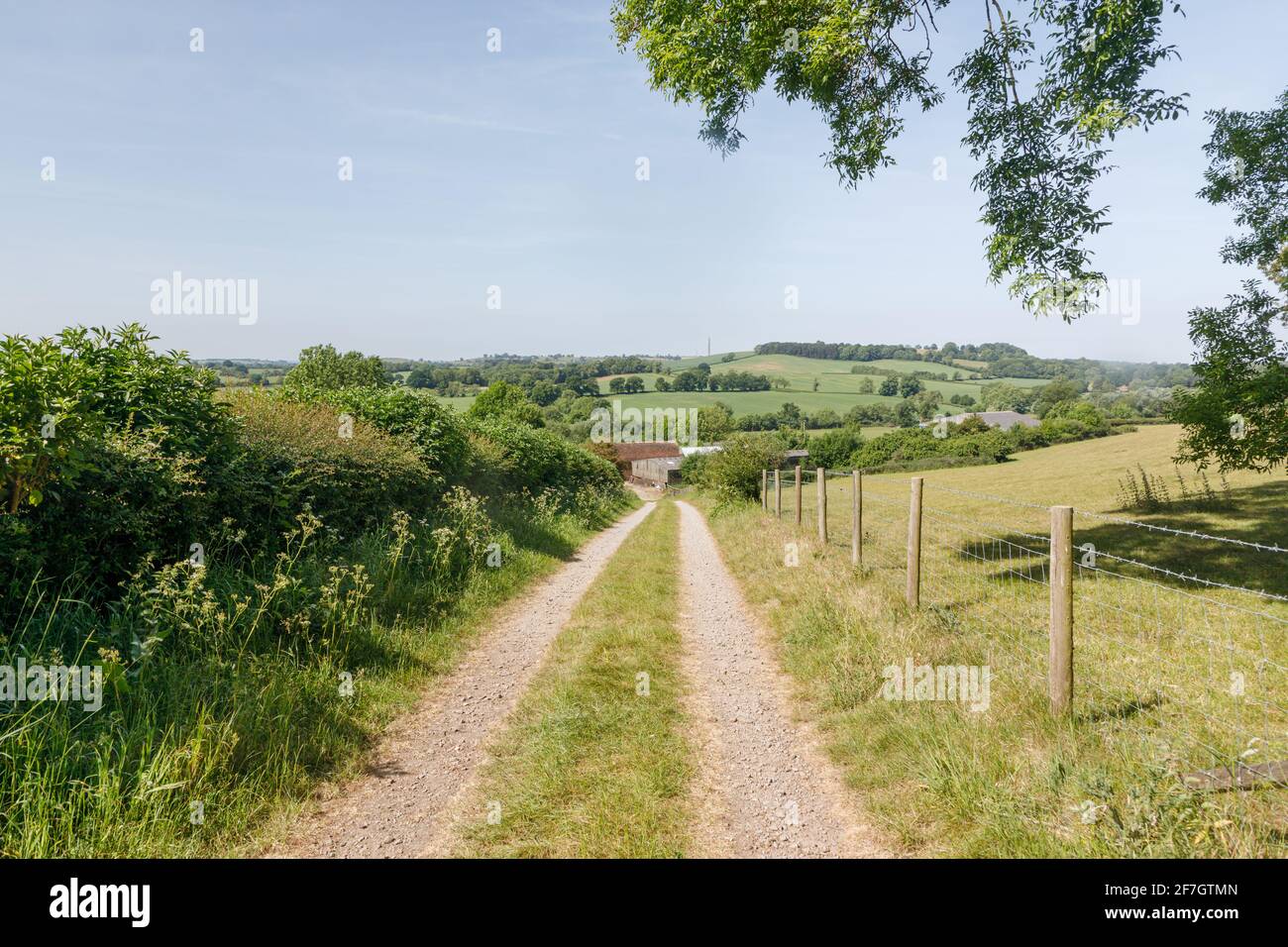 Badby, Northamptonshire, UK - May 28th 2020: An unmetalled track between a hedge and a fence leads down a hill towards some farm buildings. Stock Photo