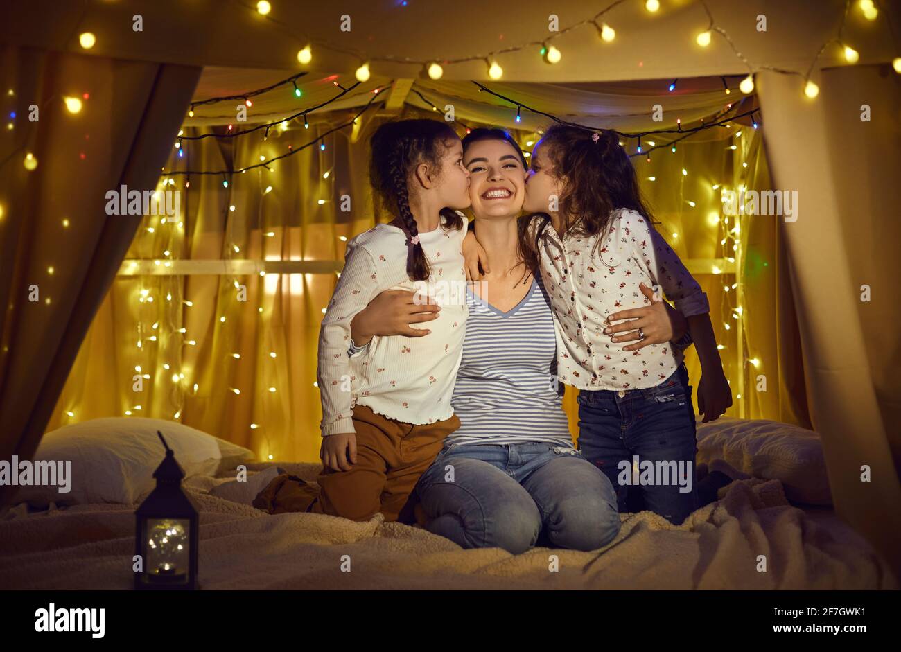 Happy daughters kissing loving mother in cheeks spend time in home tent Stock Photo