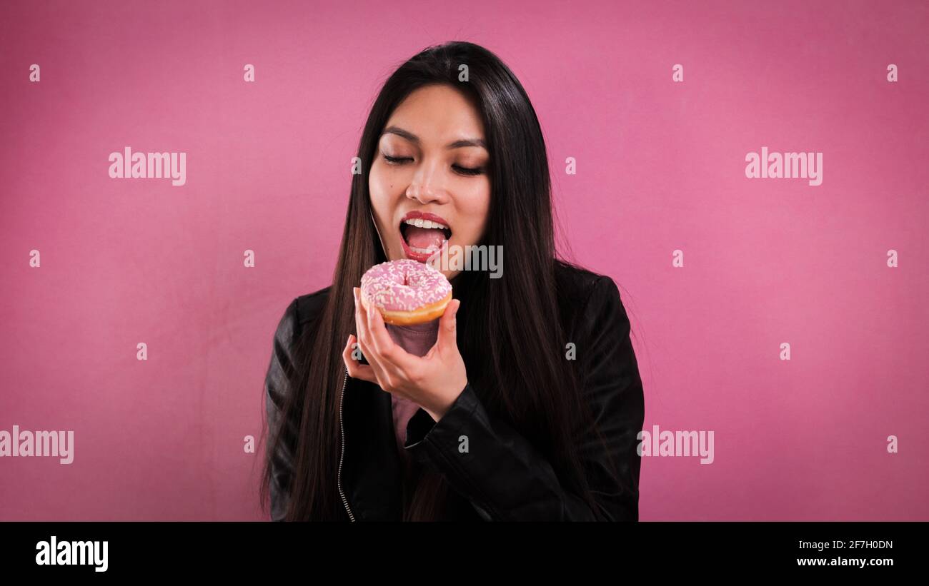 Young woman eats a doughnut against a pink background Stock Photo
