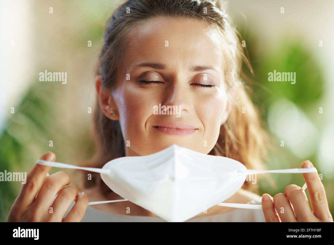 covid-19 pandemic. Portrait of relaxed trendy female in grey blouse taking off ffp2 mask. Stock Photo
