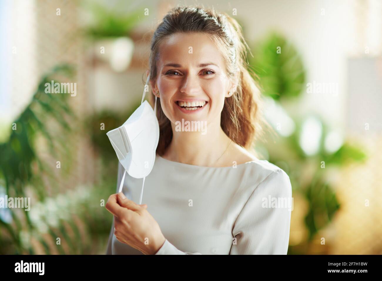 covid-19 pandemic. happy modern female in grey blouse taking off ffp2 mask. Stock Photo