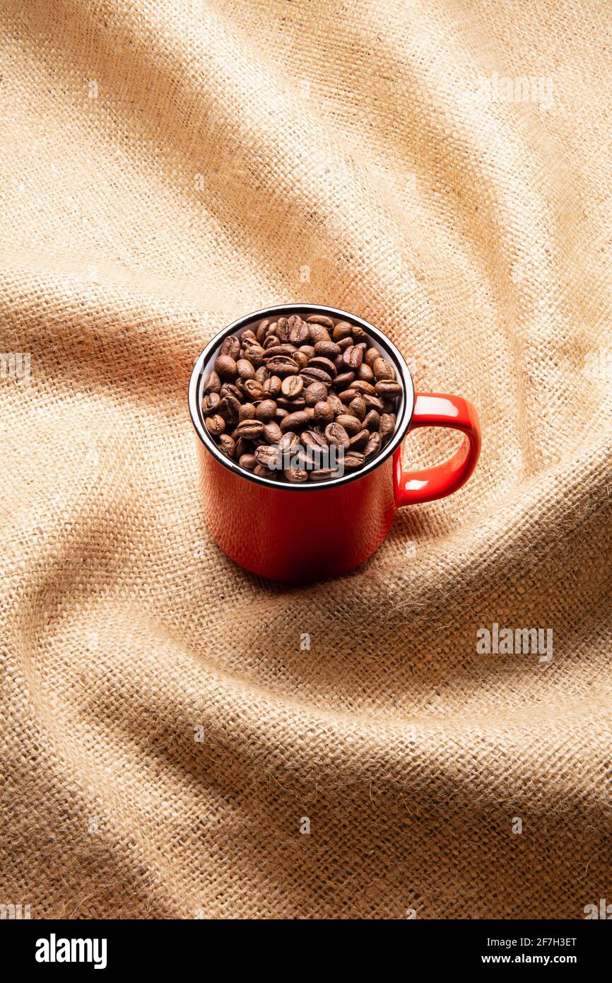 Red mug with coffee beans on twisted burlap background Stock Photo