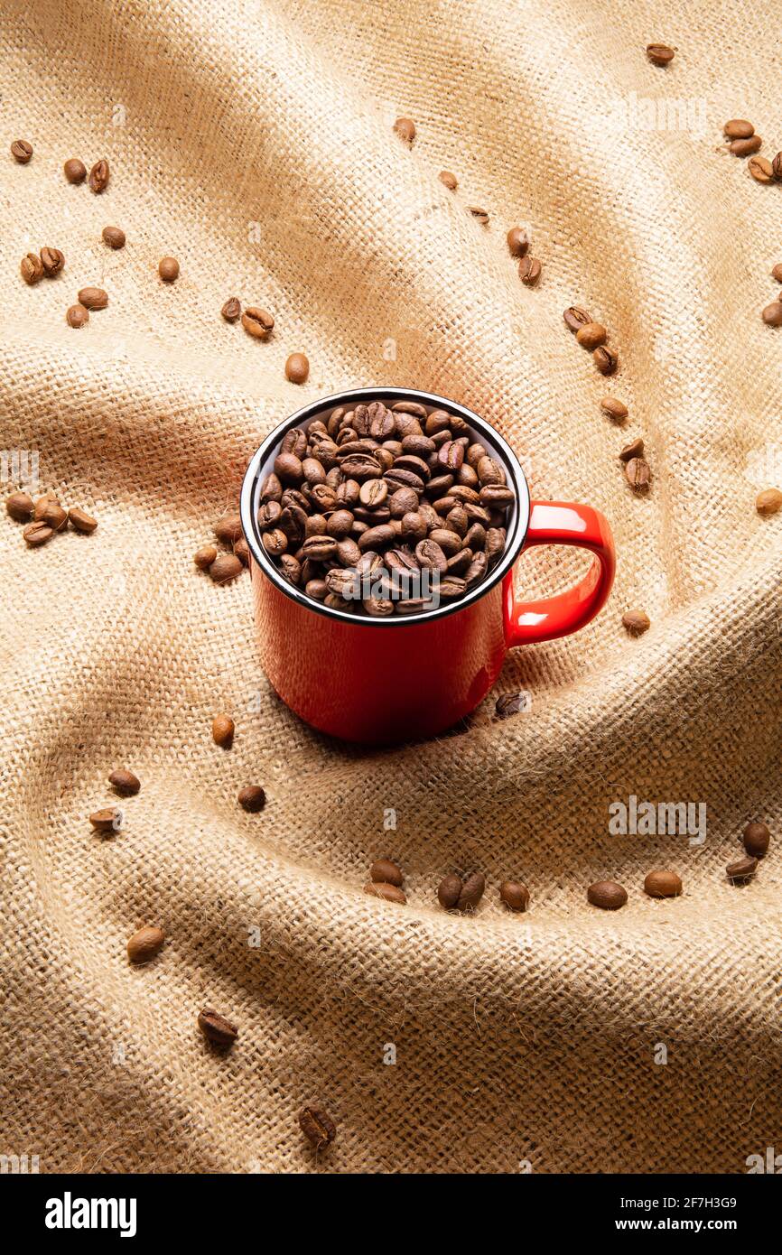Red mug with coffee beans on twisted burlap background Stock Photo