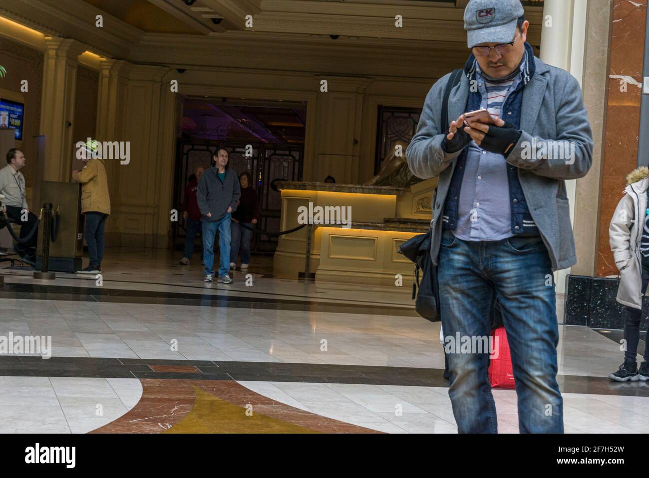 Niagara, Canada, March 2018 - Adult male of asian ethnicity stands at entrance of a reception lounge while checking or texting with his cellphone Stock Photo