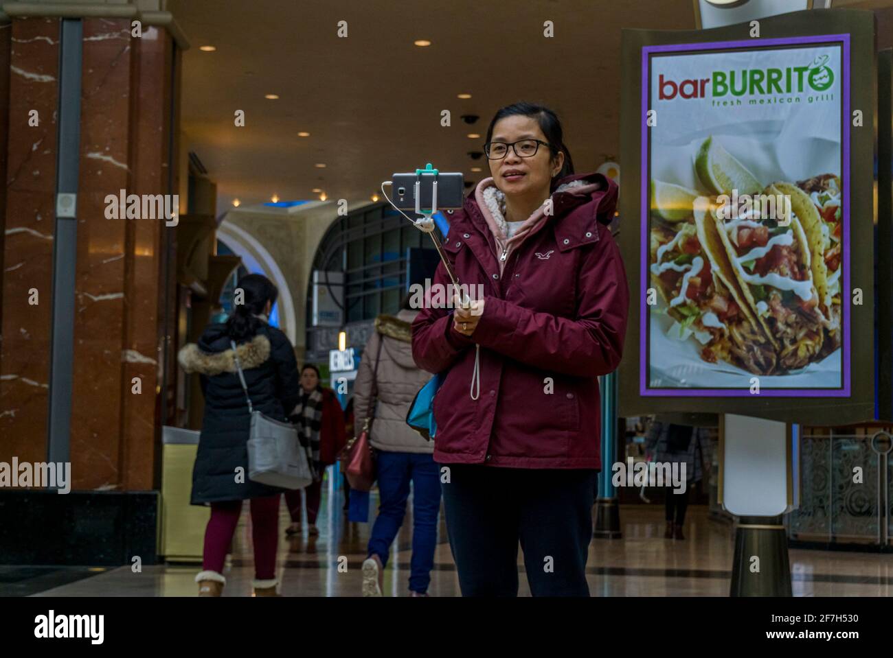 Niagara, Canada, March 2018 - Young woman of asian ethnicity takes a selfie using a stick holder, while standing inside a shopping mall Stock Photo