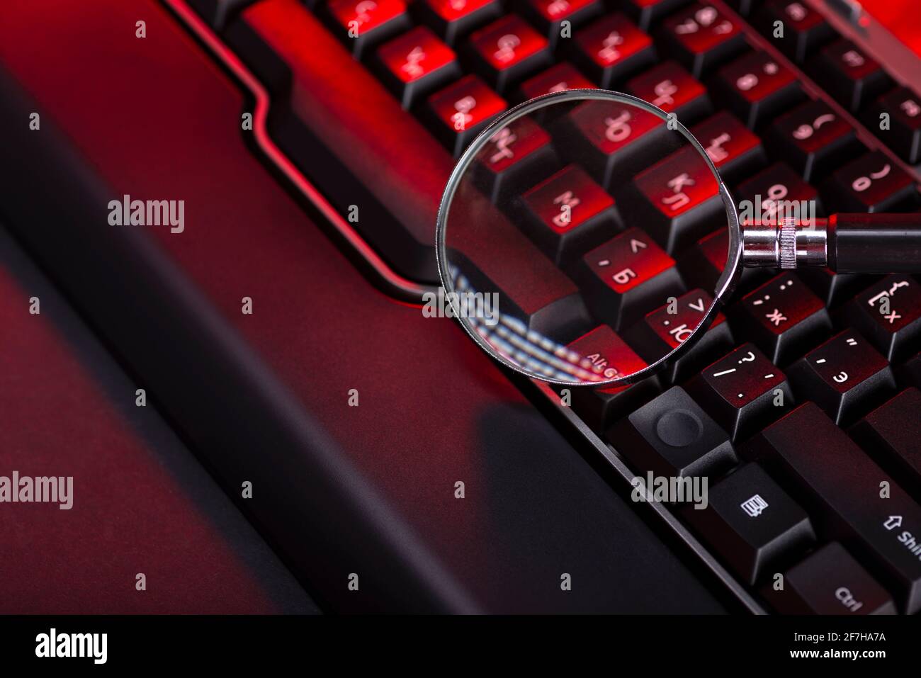 Magnifying glass on the keys of a black computer keyboard. Stock Photo